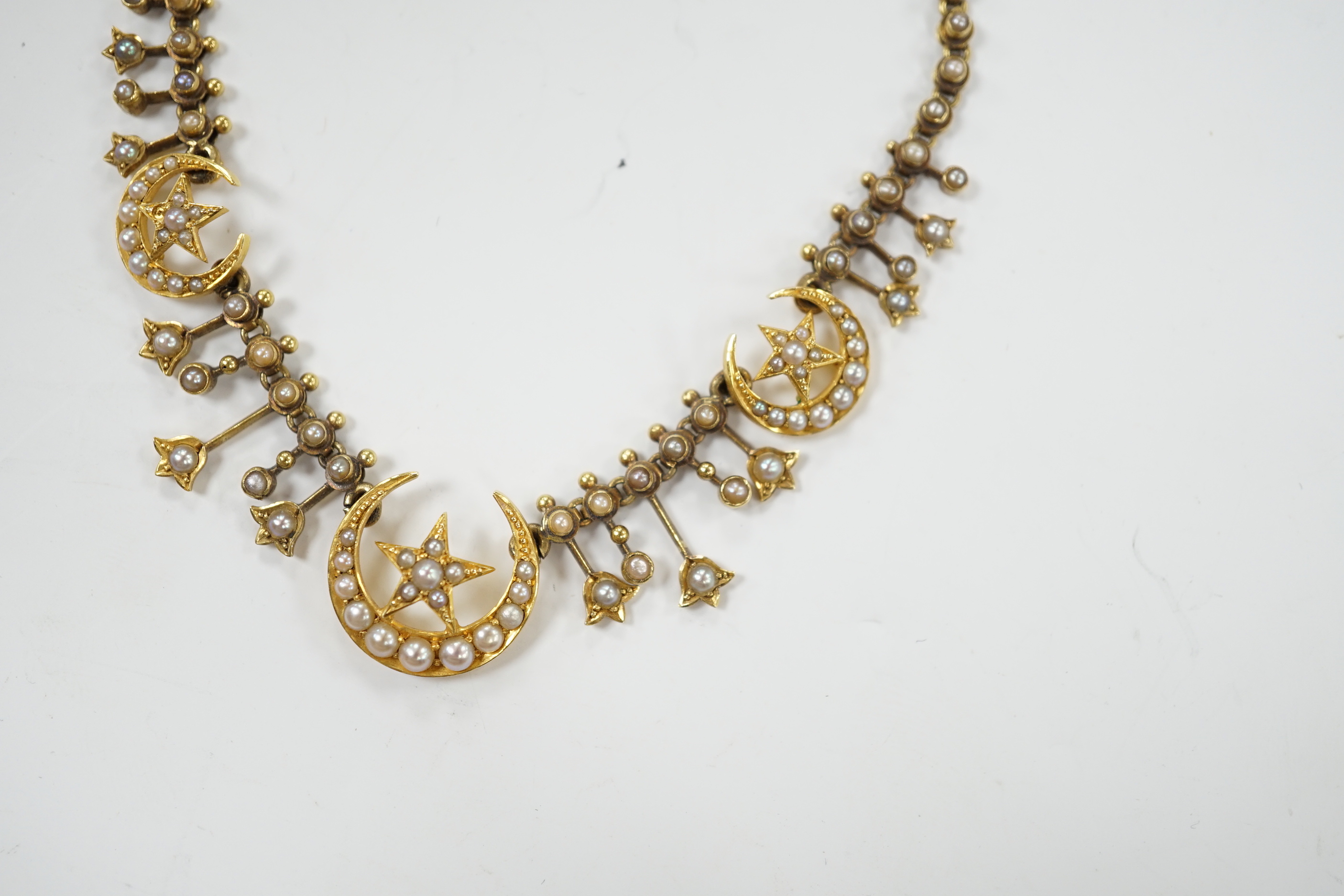 An Edwardian yellow metal and seed pearl set drop necklace, with star and crescent motifs, lacking central drop, 38cm, gross weight 16.3 grams.
